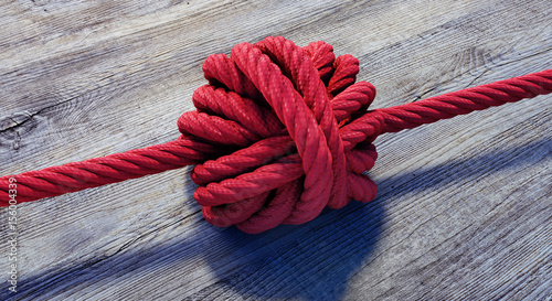 Großer Knoten in rotem Seil auf Holz photo
