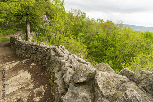 Dirt footpath with old stone wall traveling along cliff edge with green forest and landscape views