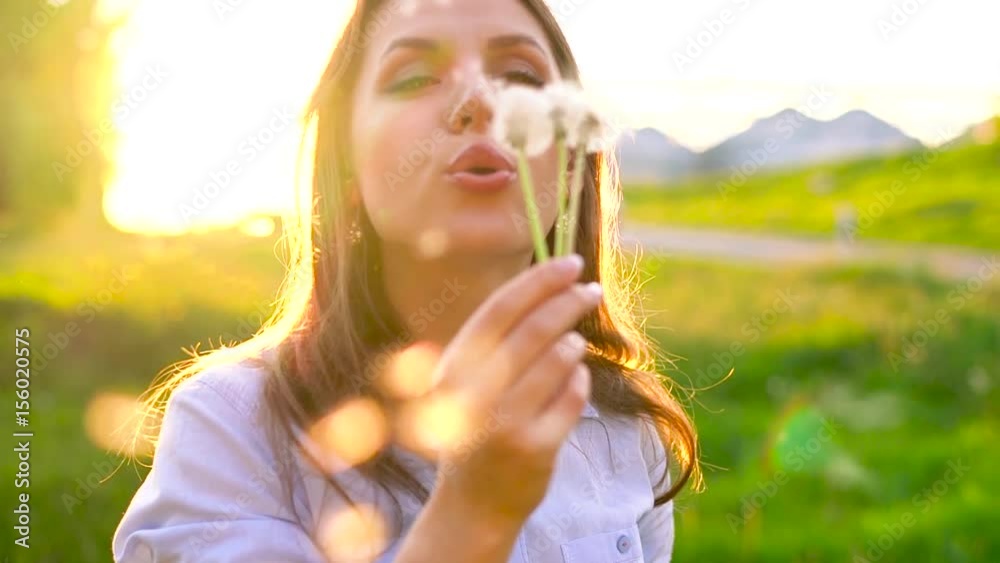 Beauty woman blowing dandelion against the sunset, slow motion