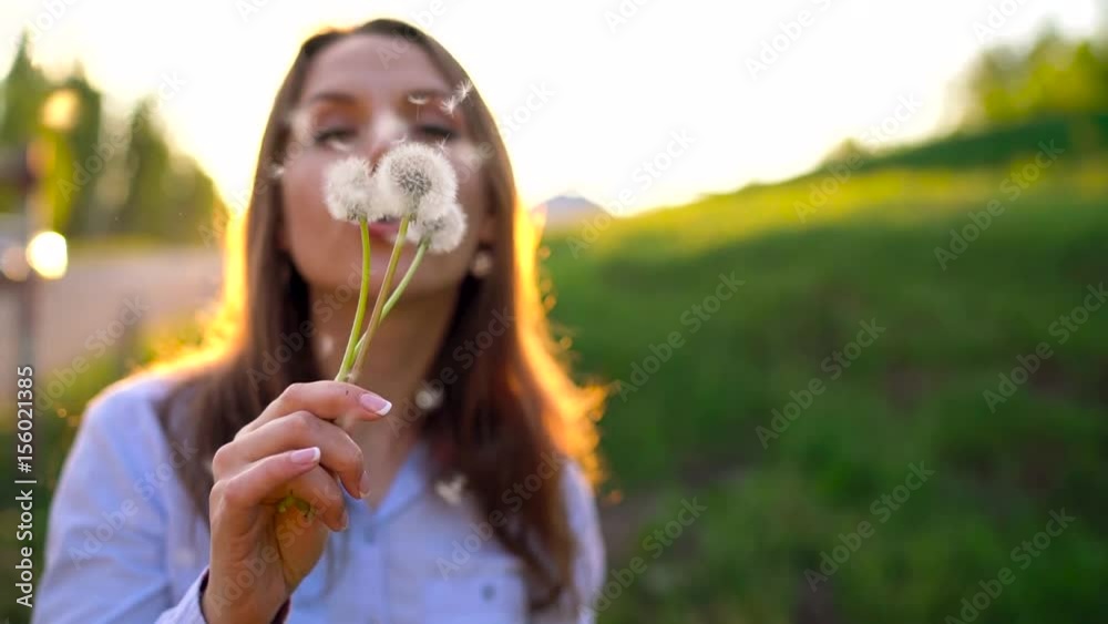 Beauty woman blowing dandelion against the sunset, slow motion