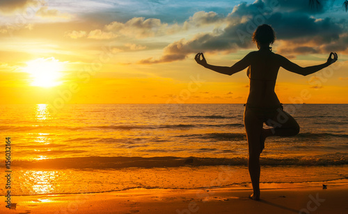 Silhouette yoga woman on sea coast at sunset.