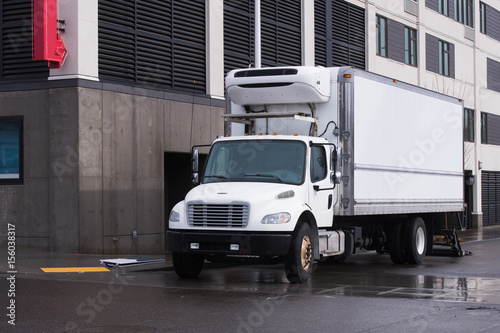 Small semi truck with reefer unit on box trailer for local delivery unloading delivered food © vit