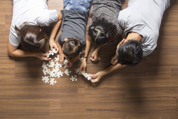Happy family top view lying on floor with solving a jigsaw puzzle problem and enjoying their leisure time activities.  in her room at home