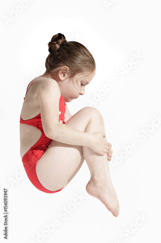 Little caucasian female diver (6 years old) jumping in diving pose  tucked his knees to his chin on white background.