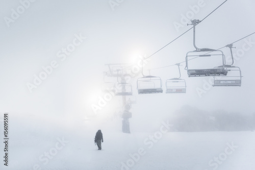 Man walking through snow with chairlift photo