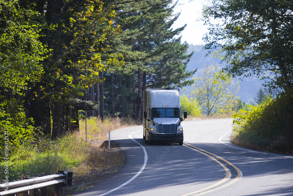 Modern semi truck on winding sunny highway with autumn trees