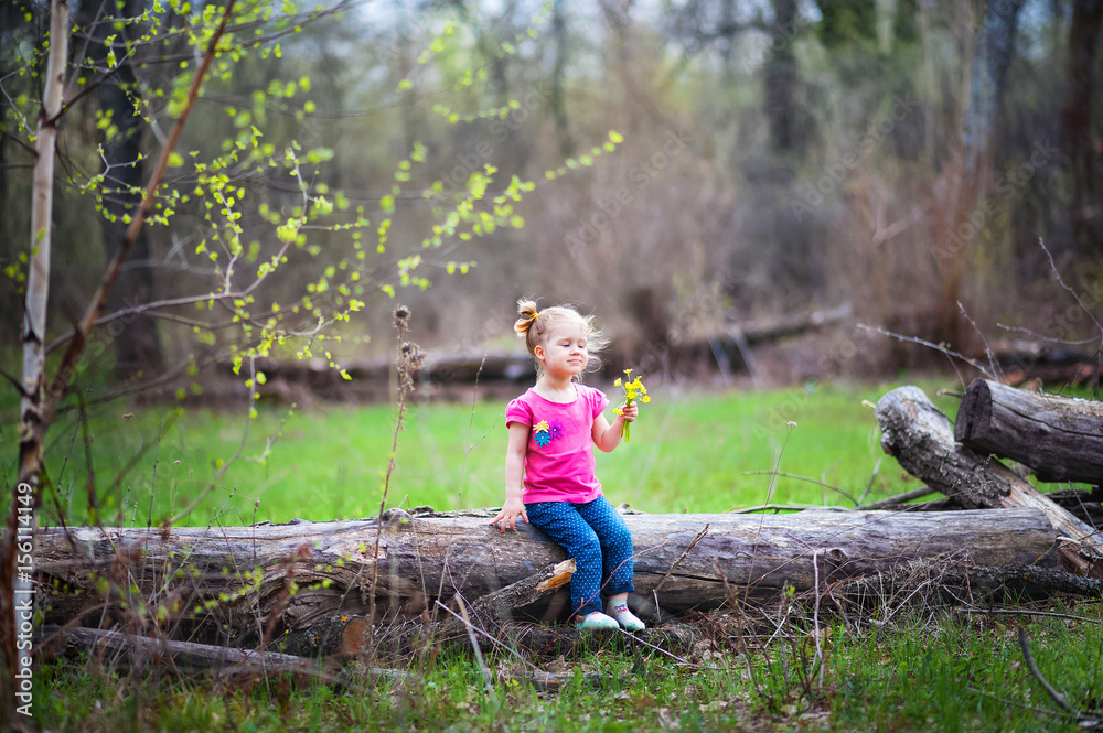 Beautiful little girl on a walk in the park in spring, summer. The girl walks through the woods, resting, having fun. A child in a pink blouse and jeans. Girl with funny tails. The girl knows the worl Beautiful little girl on a walk in the park in spring, summer. The girl walks through the woods, resting, having fun. A child in a pink blouse and jeans. Girl with funny tails. The girl knows the worl