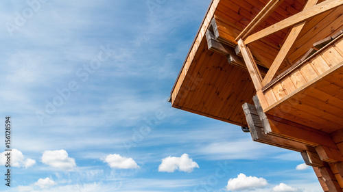 Part of the facade and roof of an ecologically clean wooden house on a background of a cloudy blue sky