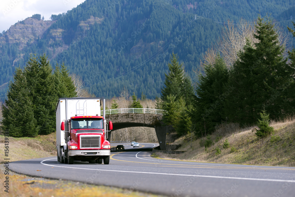 Red truck with white trailer in front of bridge Red truck with white trailer in front of bridge