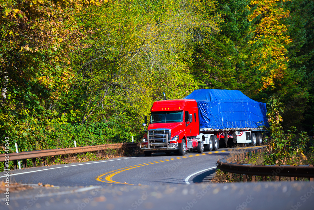 Red semi truck flat bed trailer on winding autumn highway Red semi truck flat bed trailer on winding autumn highway