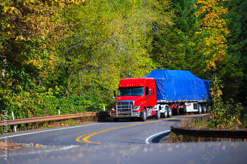 Red semi truck flat bed trailer on winding autumn highway