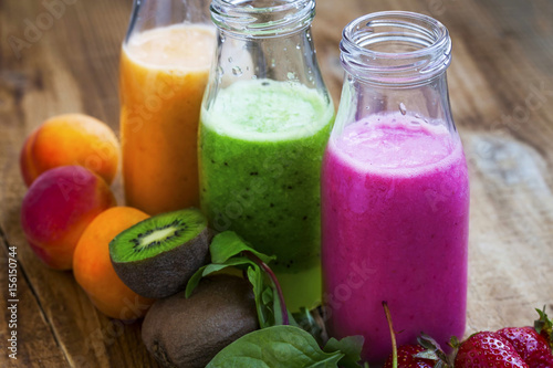 Fresh healthy three types of fruits juices or smoothies bottles  orange  green and pink with strawberries  apricots and kiwi