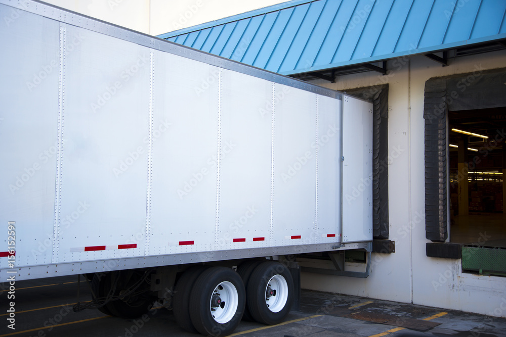 Semi trailer unloading cargo in dock warehouse with door open