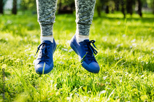Legs of a girl in sports pants and sneakers in spring grass