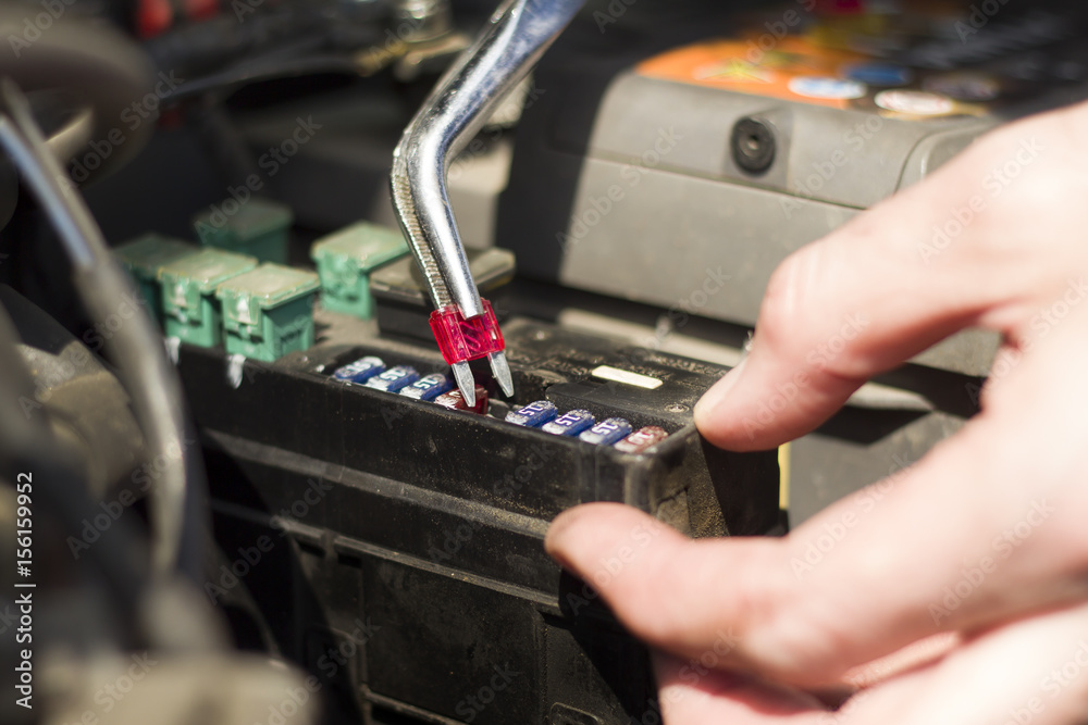 Mechanik wkłada nowy bezpiecznik do gniazda za pomocą szczypiec. Serwis samochodowy. Elektryk wymienia bezpiecznik samochodowy