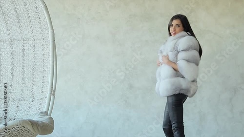 Young stylish brunette girl demonstrates fashionable arctic fox fur short coat in studio