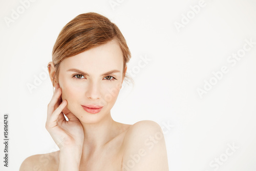 Portrait of young nude beautiful girl smiling looking at camera touching face over white background. Facial treatment. Beauty cosmetology and spa.