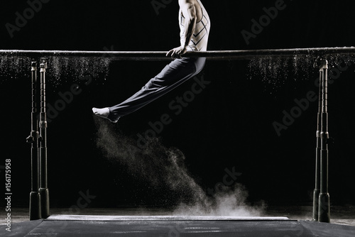 Male athlete performing handstand on gymnastic parallel bars with talcum powder. Isolated on black.