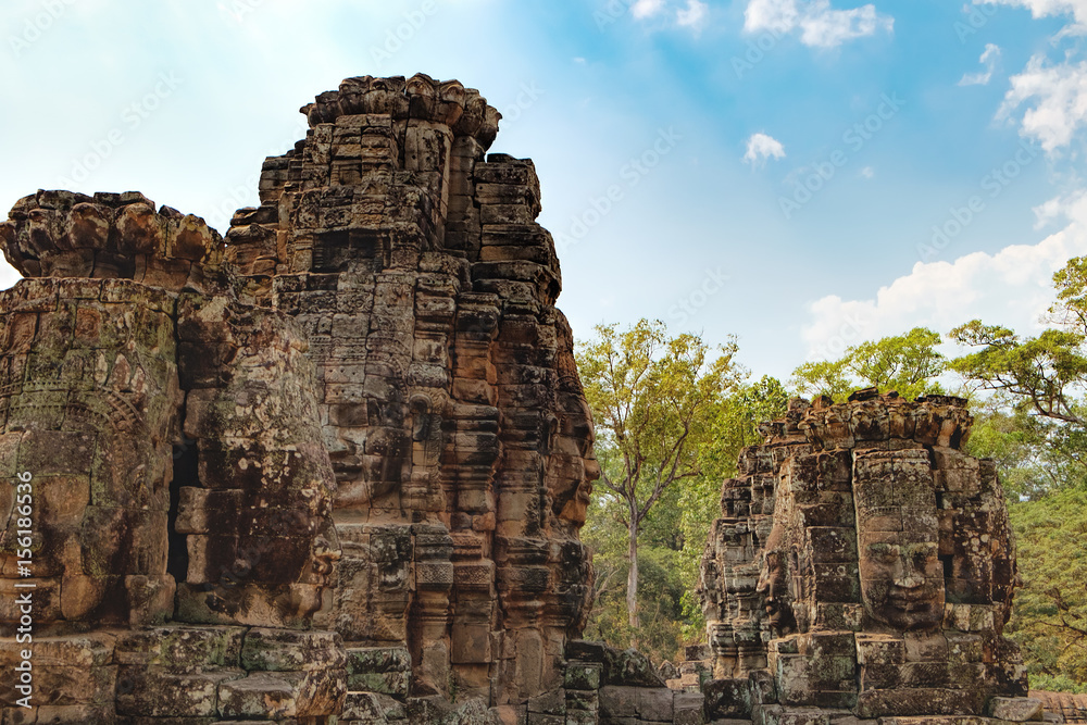 Smiling stone faces of Prasat Bayon, the central temple of Angkor Thom Complex, Siem Reap, Cambodia. Ancient Khmer temple is surrounded by tropical trees, famous Cambodian landmark, World Heritage. Smiling stone faces of Prasat Bayon, the central temple of Angkor Thom Complex, Siem Reap, Cambodia. Ancient Khmer temple is surrounded by tropical trees, famous Cambodian landmark, World Heritage.