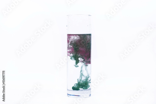 Green and pink paint fall in a glass with water