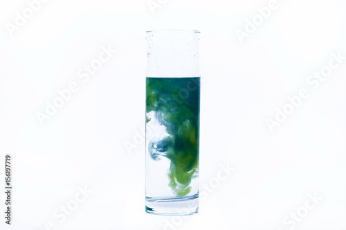 Blue and yellow paint fall in a glass with water