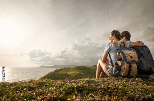Couple travelers with backpacks look sunset on coast фототапет