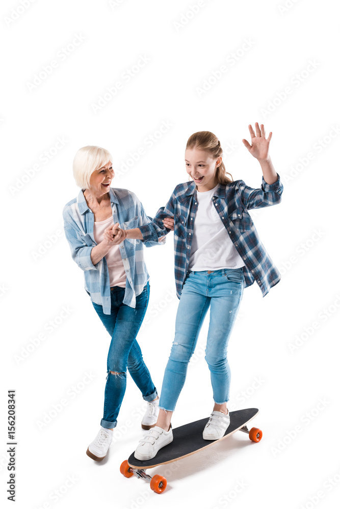 Fototapeta premium grandmother and happy granddaughter with skateboard isolated on white in studio