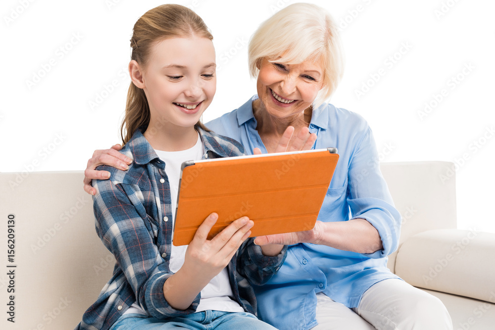 grandmother and grandchild using digital tablet and sitting on sofa isolated on white grandmother and grandchild using digital tablet and sitting on sofa isolated on white