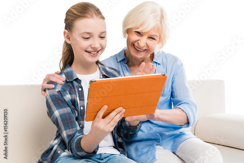grandmother and grandchild using digital tablet and sitting on sofa isolated on white