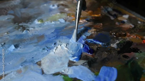 The artist mixes oil paints with a brush on the palette closeup