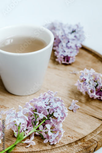 Lilac flower and a cup of tea on the wood delivery desk. White background.