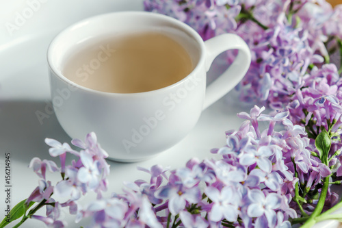 Springtime. Cup of tea and lilac morning bouquet on the table. White background.