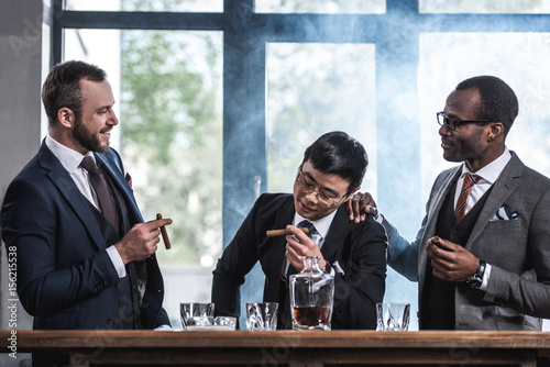 multicultural business team spending time, smoking cigars and drinking whiskey photo