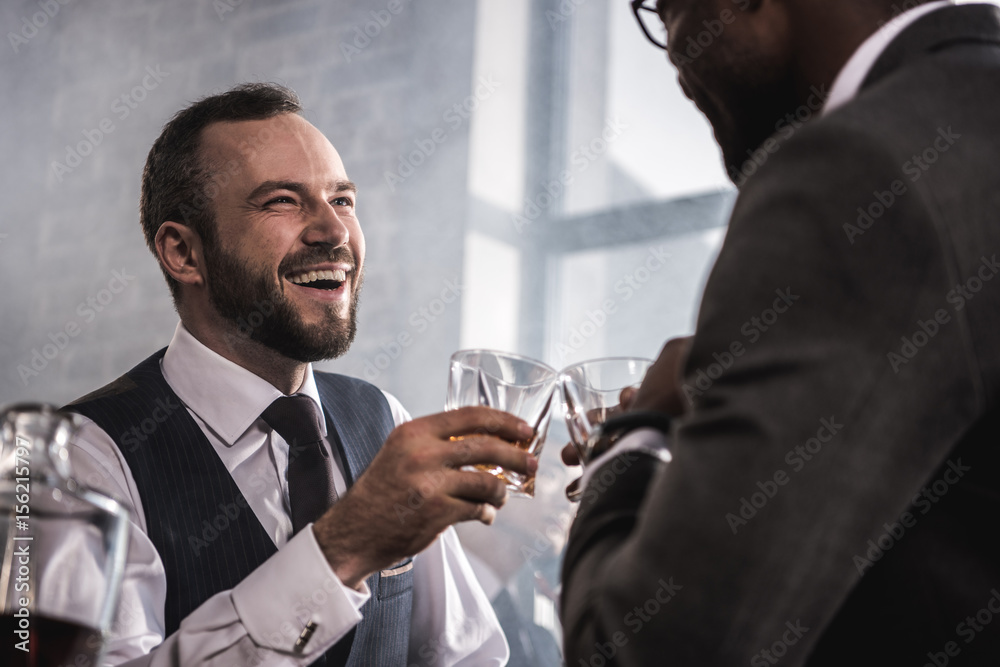 Two businessmen in formal wear clinking whiskey glasses and talking Two businessmen in formal wear clinking whiskey glasses and talking