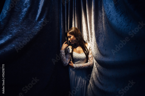 The beautiful girl has a white dress and stands near wall with tissue © myronovychoksana