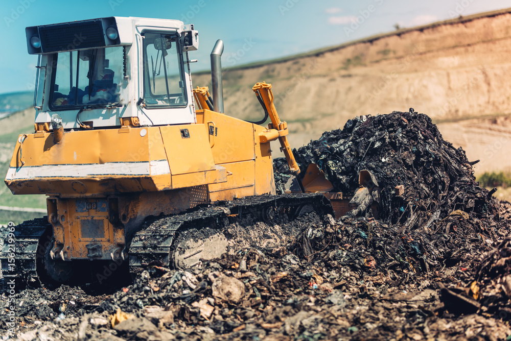 Industrial bulldozer pushing garbage and working on trash site