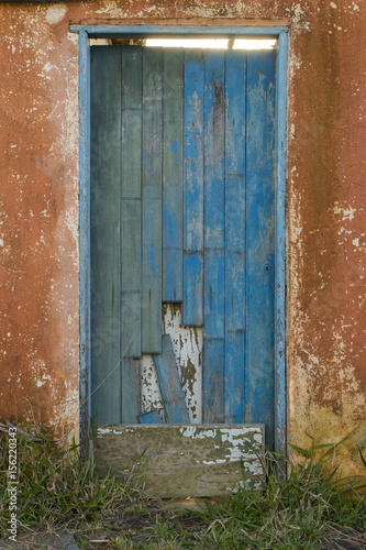 old blue wooden door on an orange wall in an abandoned house - vertical © Guilherme
