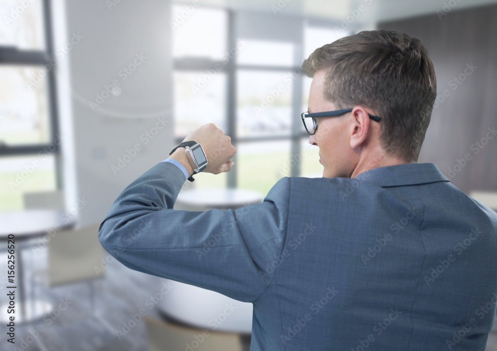 Businessman holding arm with watch to eyes in office