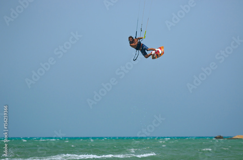Professional kite boarding rider sportsman jumps high acrobatics kiteboarding trick with raley from water. Recreational activity and extreme active water sports, hobby and fun time