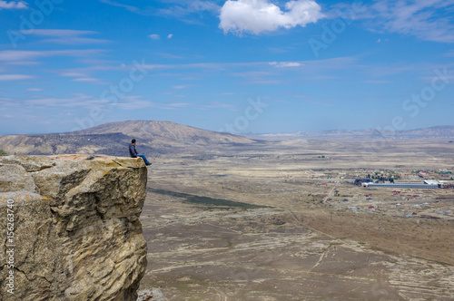 Tourist sit on the edge of cliff and look at panoramic view of Gobustan from Kichikdash mountain. Azerbaijan