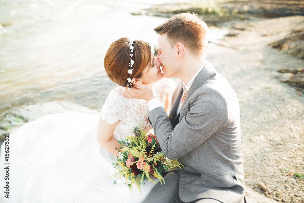 Bride and groom holding beautiful wedding bouquet. Posing near river Bride and groom holding beautiful wedding bouquet. Posing near river