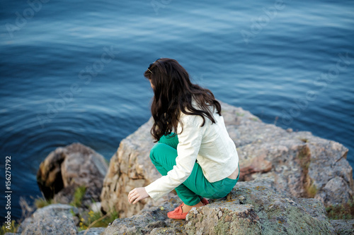 woman sits on the rock and enjoys the view of the river 