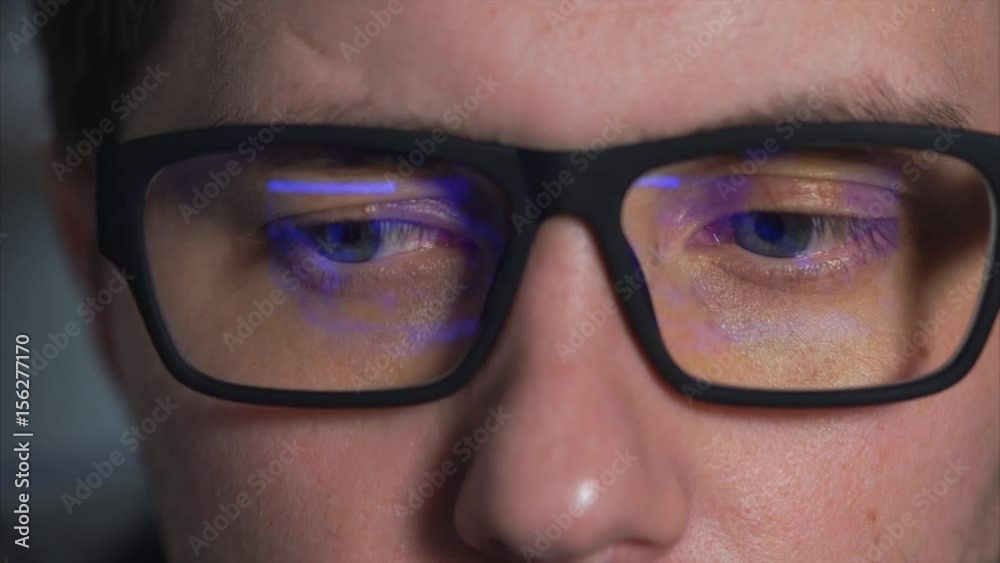 close up shot of the eyes of a young man wearing glasses who is watching a movie on a computer monitor. The video is reflected in the glasses of his glasses, the person looks closely close up shot of the eyes of a young man wearing glasses who is watching a movie on a computer monitor. The video is reflected in the glasses of his glasses, the person looks closely