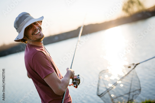 Young man fishing on a lake at sunset and enjoying hobby photo