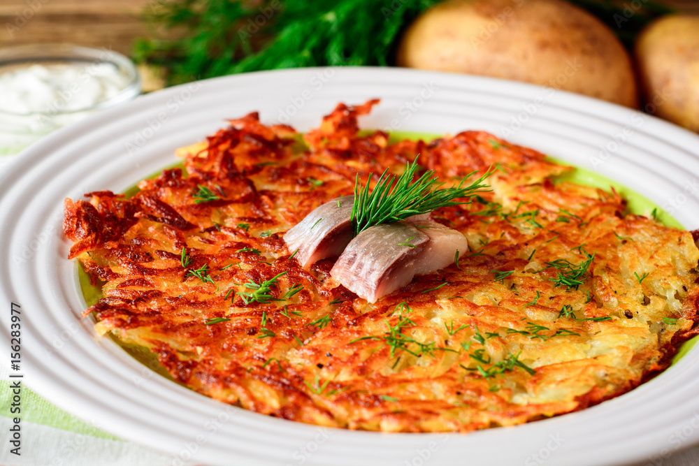 Potato rosti with dill and salted herring in plate on wooden table.