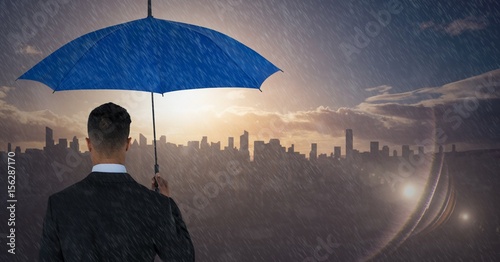 Back of business man with umbrella against skyline with sunset