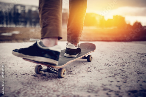 Man male skateboarder on a skateboard is riding in the sunset on the road, close-up. Concept street sport in holey boots. © Parilov