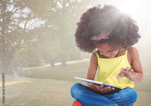 Girl with tablet against blurry park with flare