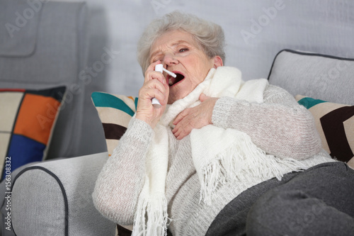 Senior ill woman using spra...