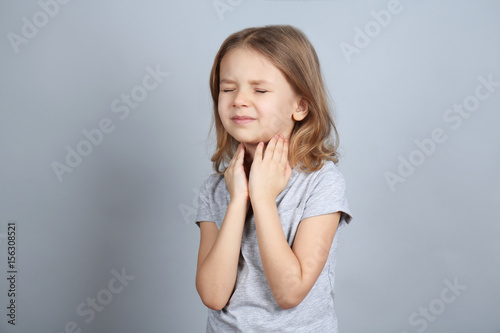 Little ill girl with sore throat on color background. Concept of allergy